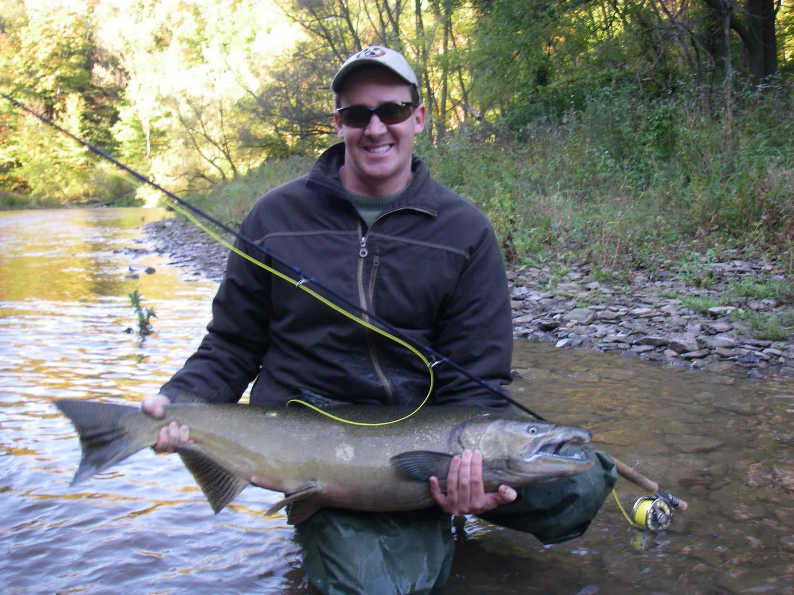 An angler holding a chinook salmon beside a fly rod on Bronte Creek in fall