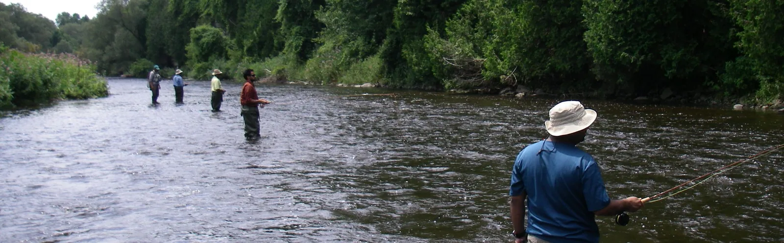 A group of anglers spread across a summer river, casting, during an on-the-water session