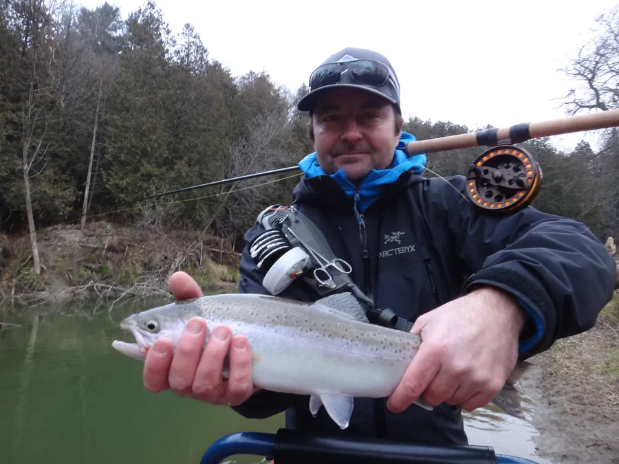 An angler holding a steelhead with a fly reel and rod visible
